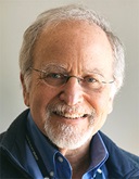 An older man with glasses smiles at the camera for his headshot.