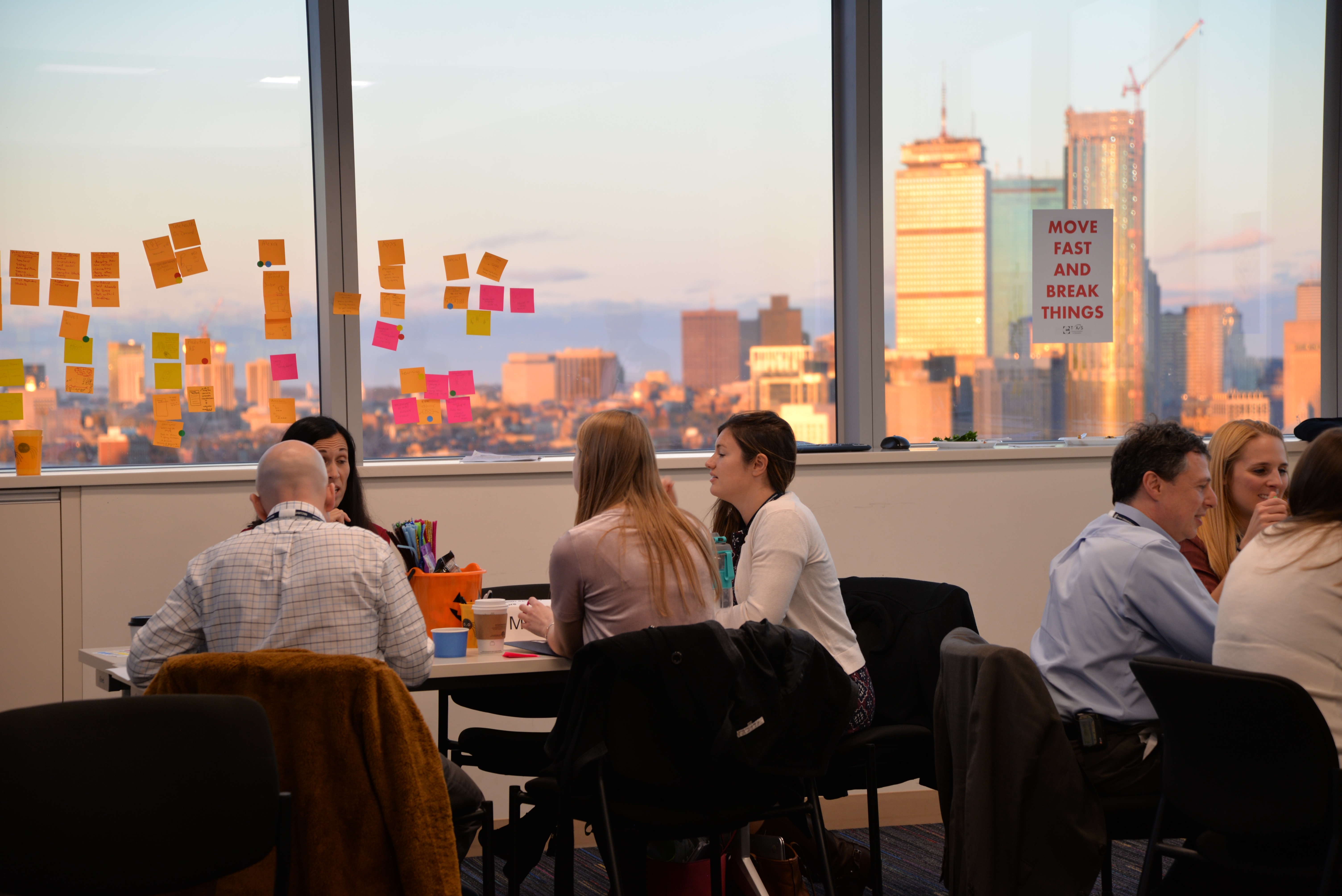 A team of people in an office setting next to a window with a sign that says work fast.