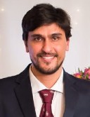 A man, Tiago Koppe, wears a suit with a red tie.