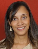 Marcela Oliveira, a woman with brown hair leaves it down while she smiles at the camera for her headshot.