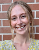 McKena Geiger, a blonde woman with her hair in a ponytail smiles at the camera for her headshot.